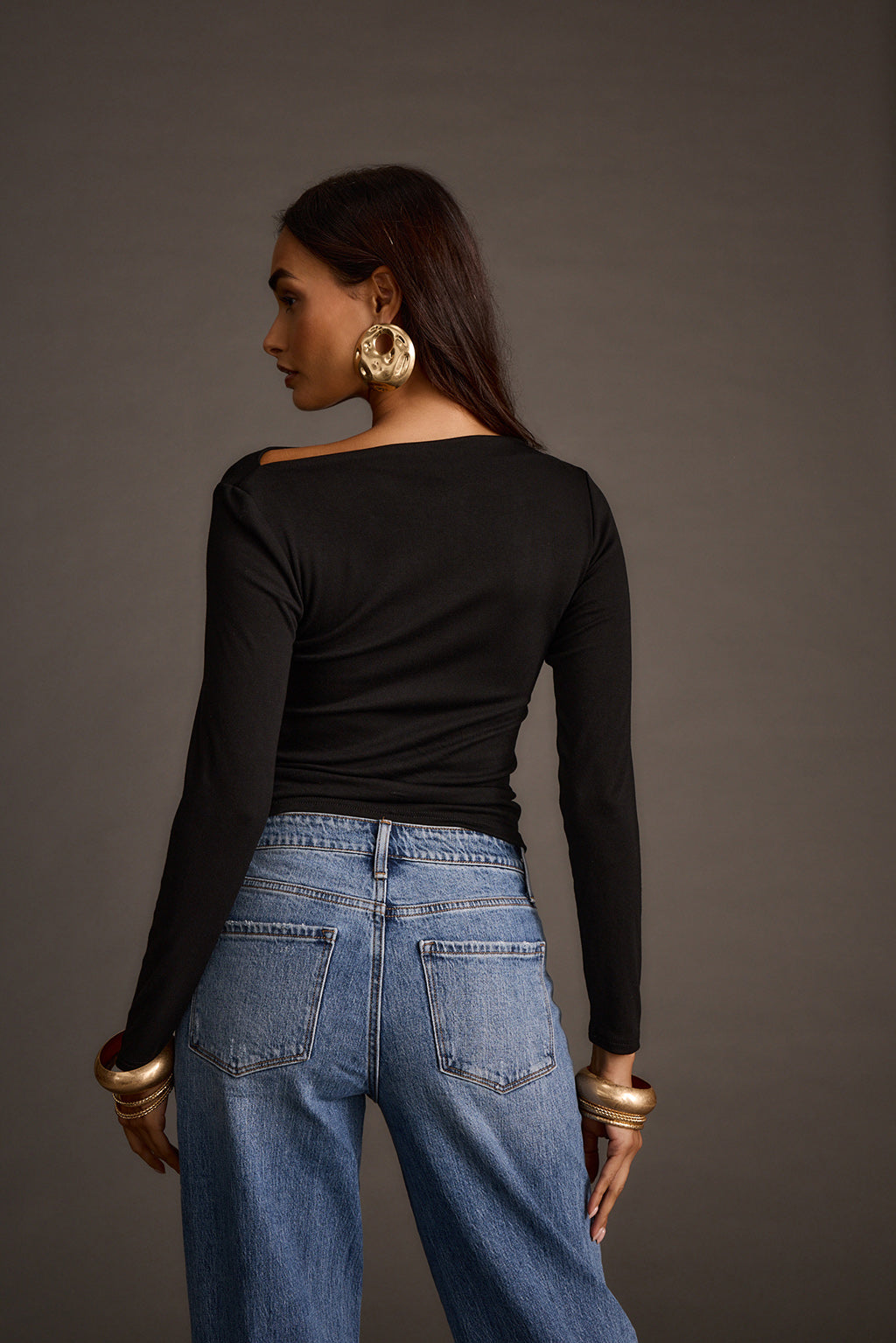 Back view of a black off-the-shoulder top paired with wide-leg jeans and gold cuffs