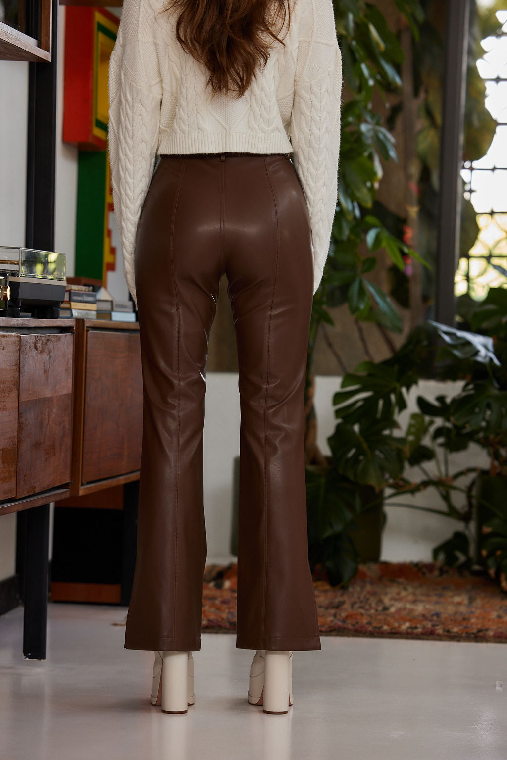 Back view of brown vegan leather flare pants showing seam detail, styled with cream heels.
