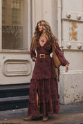 Woman wearing a burgundy maxi dress with a tiered skirt and fringe bag on a city sidewalk