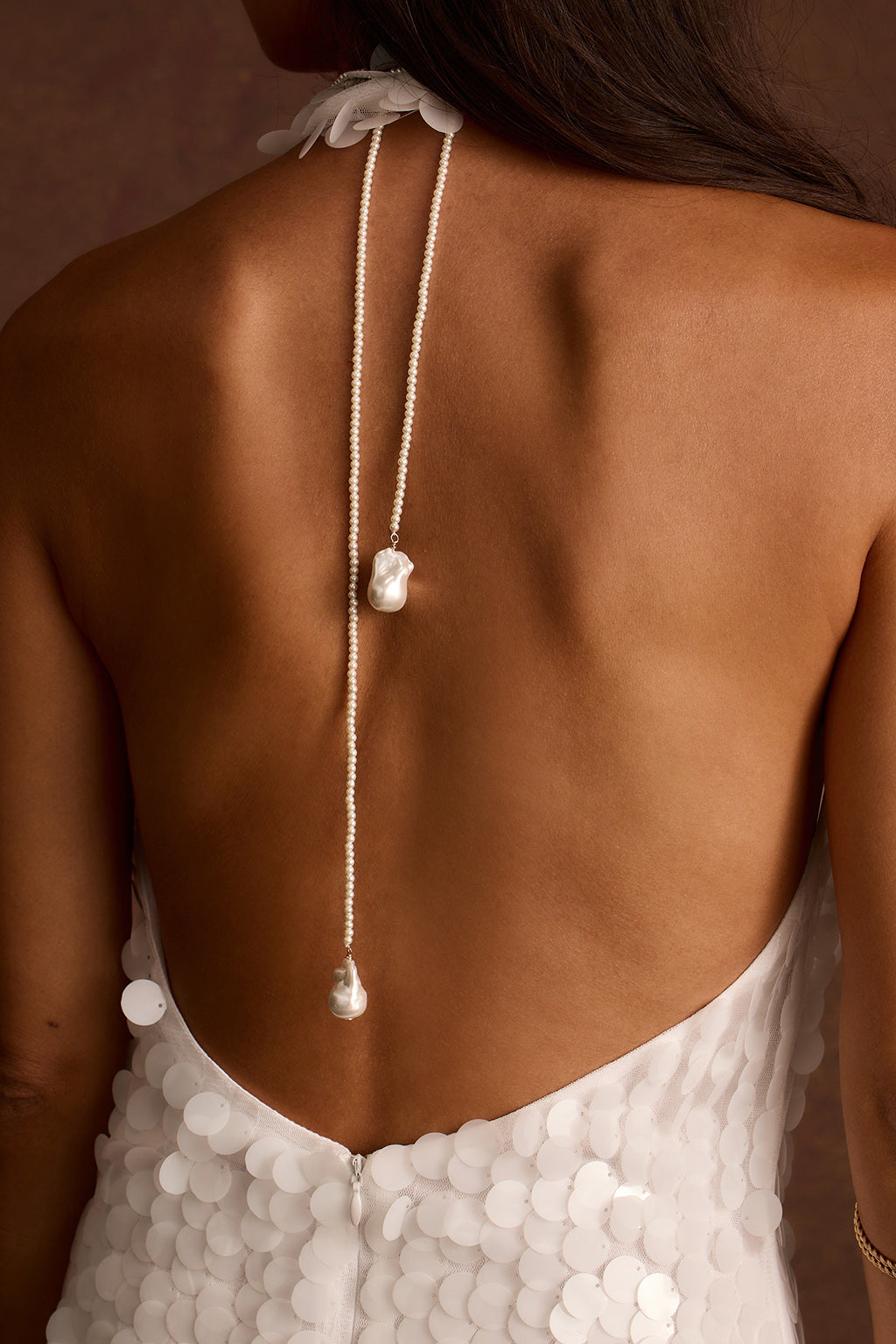 Pearl lariat necklace with a baroque pearl drop draped down the back, worn with a white sequin gown.