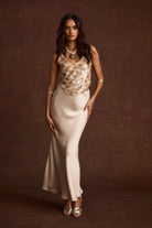 Model wearing the 12th Tribe Dolce Champagne Satin Maxi Skirt in soft champagne, featuring a high-waisted silhouette with a flowing, floor-length hem, styled with a cropped top and strappy heels for weddings, brunches, and evening events