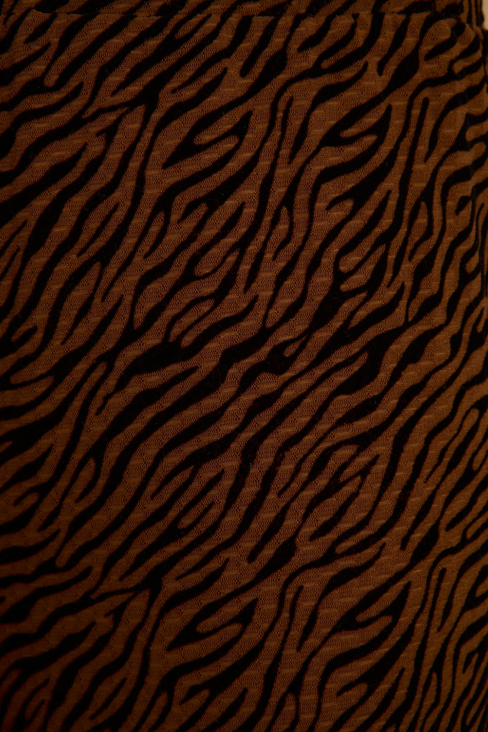 Close-up of cognac and black zebra print fabric on the Silver Springs flare pants showing bold animal stripe texture.