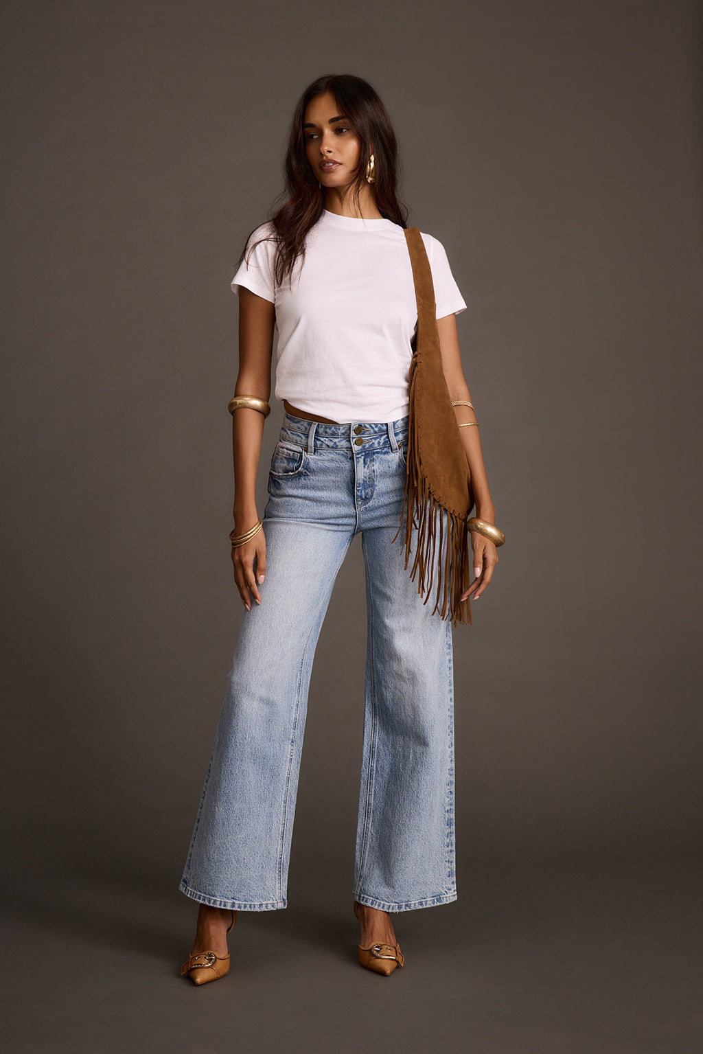 Woman wearing light-wash flare denim jeans with a white t-shirt and fringe shoulder bag