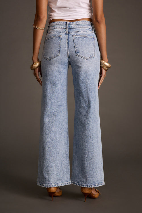 Women's light-wash flare denim jeans styled with brown heeled sandals, back view