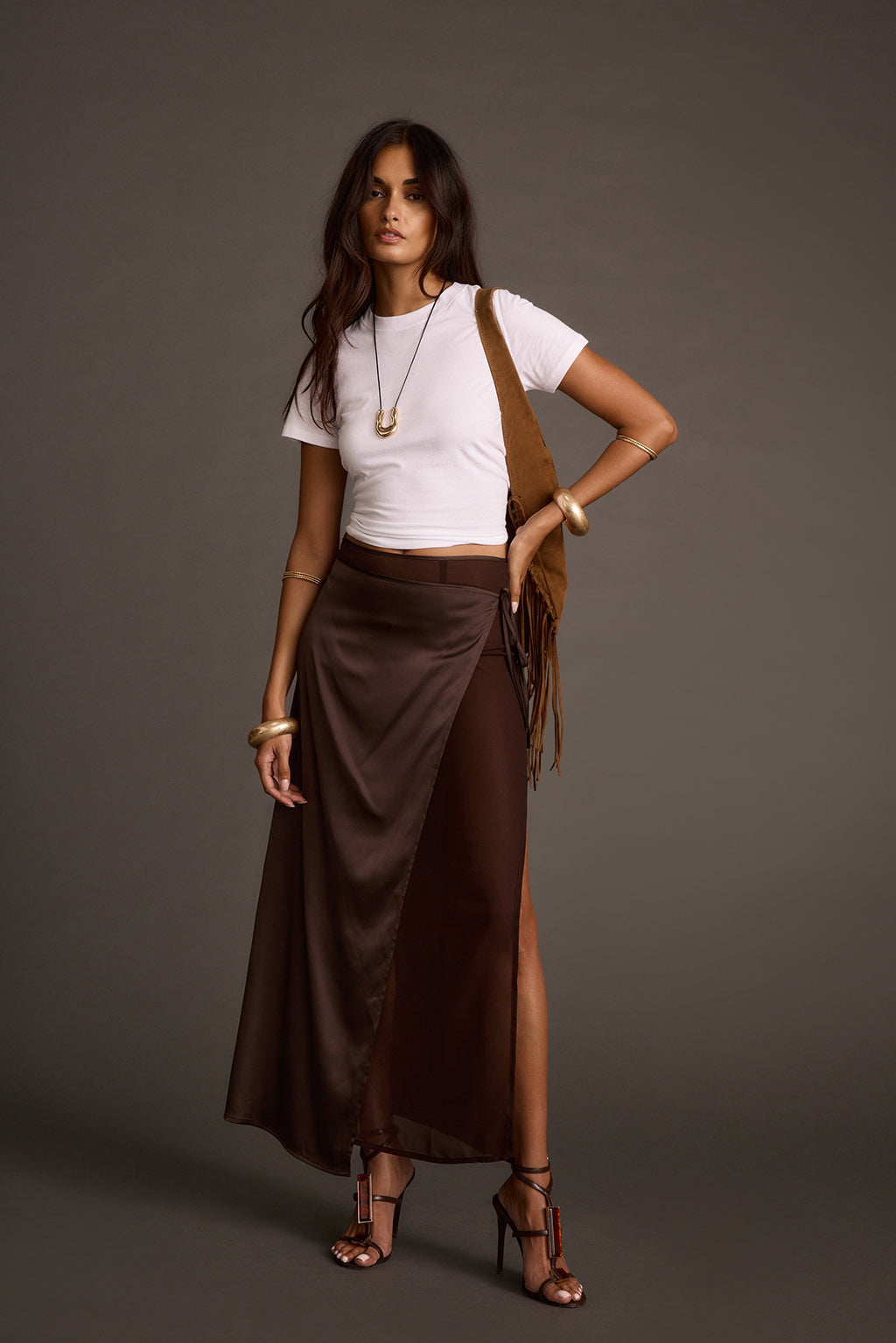 Woman wearing a brown satin wrap maxi skirt with a white cropped tee and fringe shoulder bag