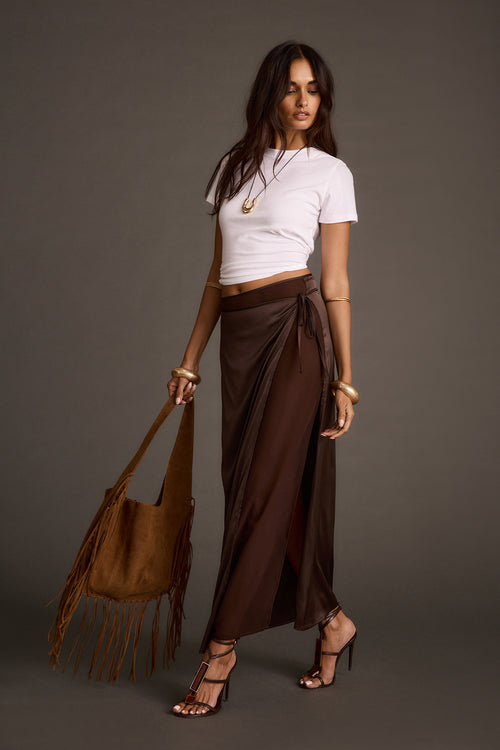 Full-length front view of a brown satin tie maxi skirt worn with a white crop top and brown suede fringe tote