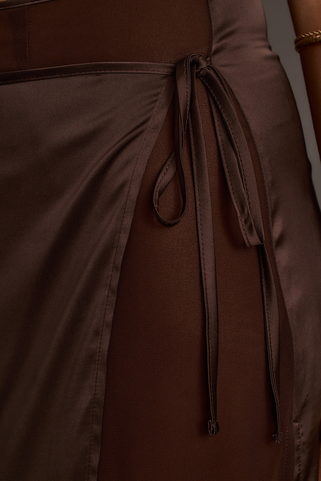 Close-up of a brown satin tie maxi skirt showing the side tie detail and fabric sheen