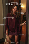 Woman wearing a burgundy cape top with a matching lace mini skirt, gold hoop earrings, a layered pendant necklace, gold bangles, and a gold mesh bag, with text reading Shop the Full Look and labels naming each piece