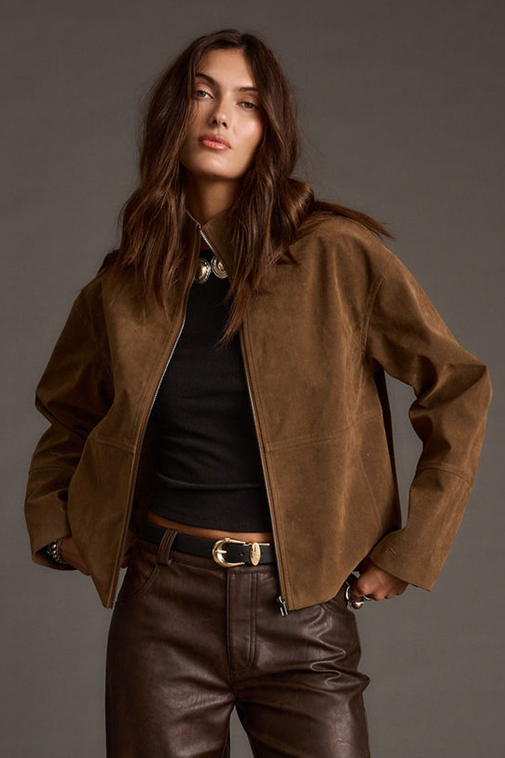 Woman wearing a brown suede jacket and pants against a gray background