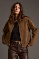 Woman wearing a brown suede jacket and pants against a gray background