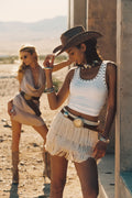Model wearing the 12th Tribe Sunwoven Natural Fringe Mini Skirt, a mid- to high-rise skirt featuring layered fringe detailing over a crocheted base layer, perfect for summer soirées, festival-ready looks, and stylish warm-weather outfits