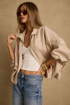 Model wearing the 12th Tribe Monte Khaki Bubble Hem Jacket, featuring a relaxed fit with bubble hem detailing, styled with the Muse Barrel Denim Jeans, Emily White Ribbed Halter Top, and Runyon Set of 2 Gold Cuff Bangles.