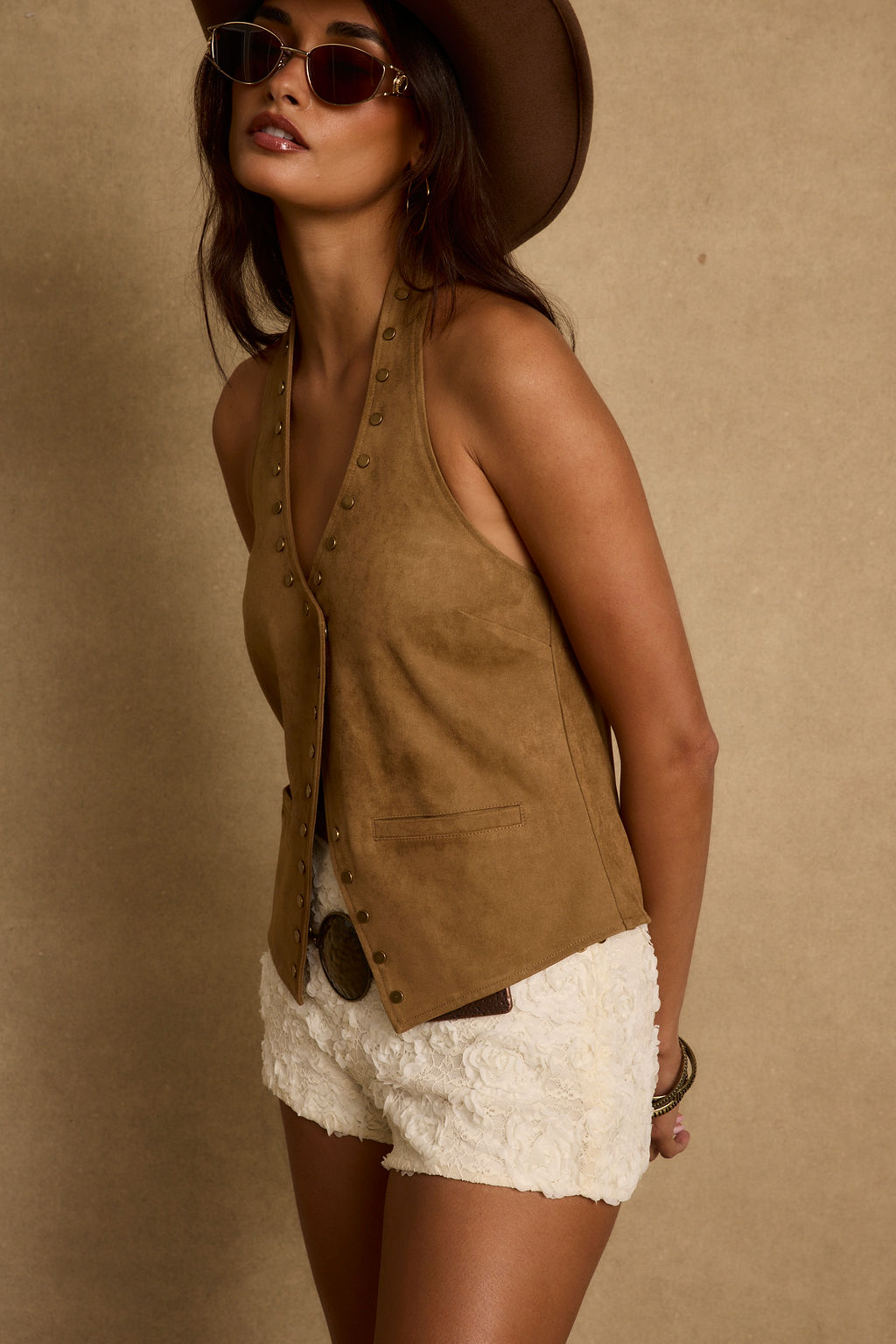 Tan suede button-up vest and white quilted shorts with a brown cowboy hat with rose-gold sunglasses