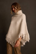 Women's poncho in cream knit with turtleneck and fringe hem, three-quarter angle on model