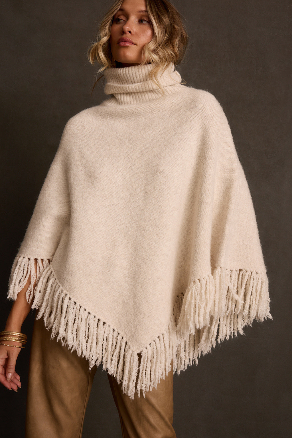 Cream poncho back view showing draped shape and thick yarn fringe along hem edge