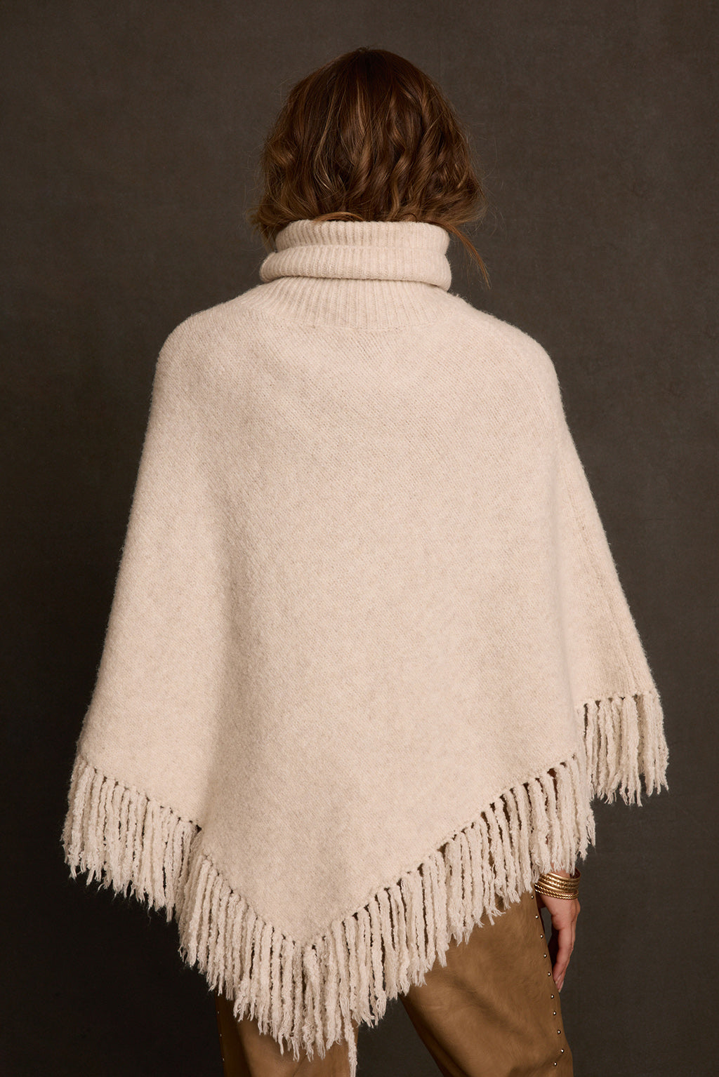 Turtleneck poncho styled over cable knit sweater dress with cream boots and gold jewelry