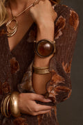 Gold cuff bracelet with large amber cabochon stone, close-up on wrist with stacked bangles