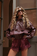 Woman wearing a cropped burgundy faux-leather jacket with matching satin lace-trim shorts