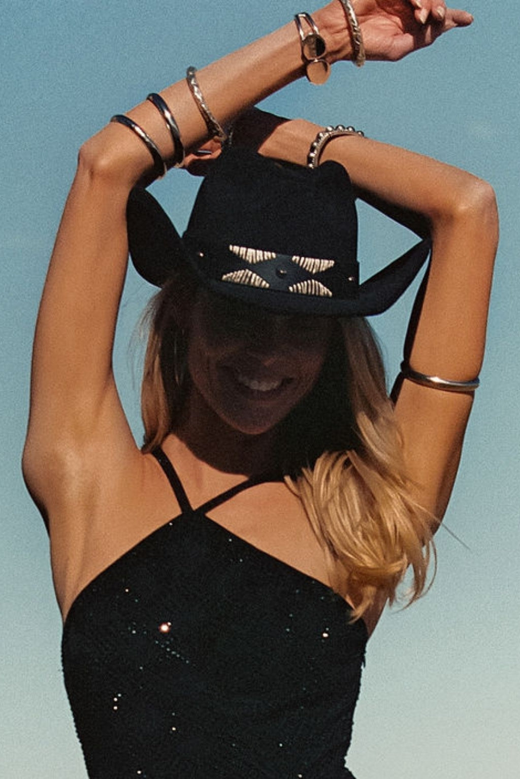 Model wearing the 12th Tribe Talon Black Suede Cowboy Hat, a western-inspired hat in soft black suede featuring an adjustable sweatband for a custom fit, gold stud and embroidered hat band, and a curved, rolled brim, perfect for adding a stylish, festival-ready touch to casual outfits, summer looks, and vacation ensembles