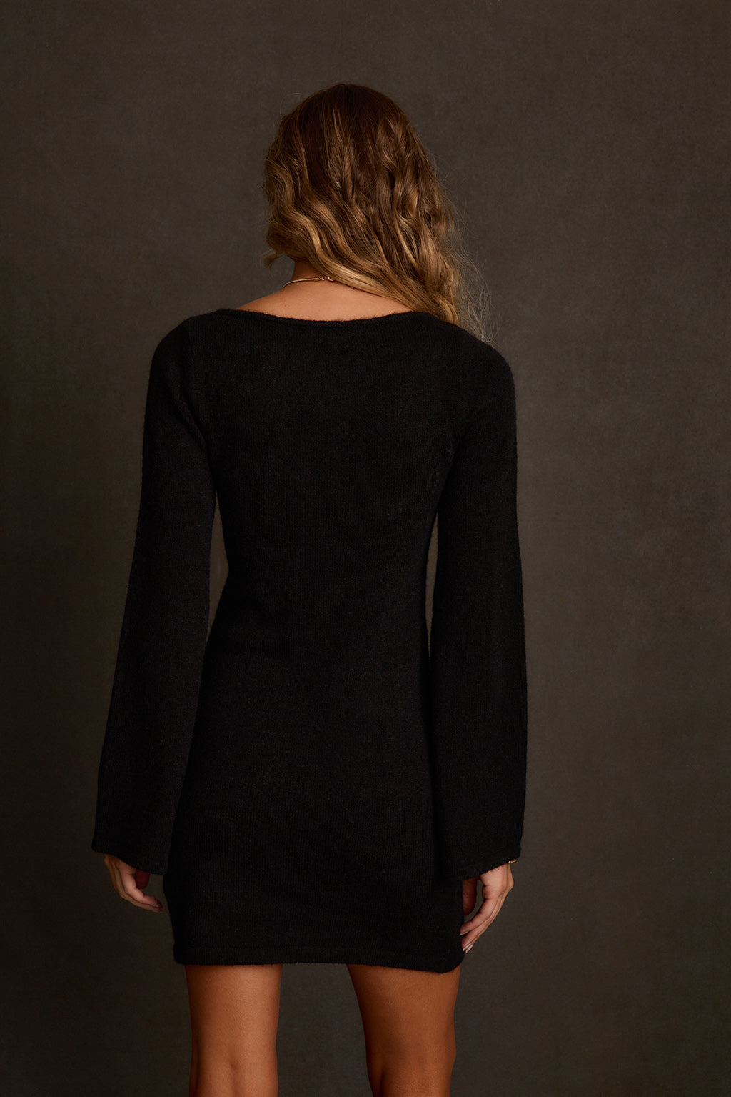 Women's mini dress front view showing fitted silhouette and long bell sleeves in black knit