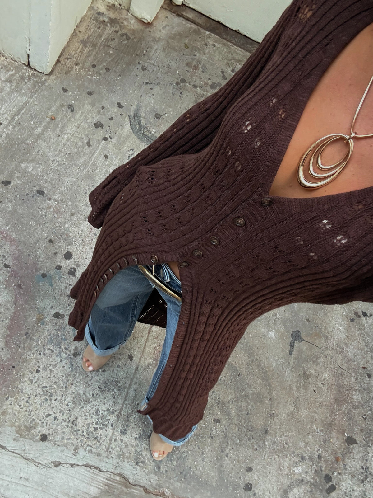Overhead shot of a woman wearing a brown ribbed knit cardigan over jeans with a silver pendant necklace