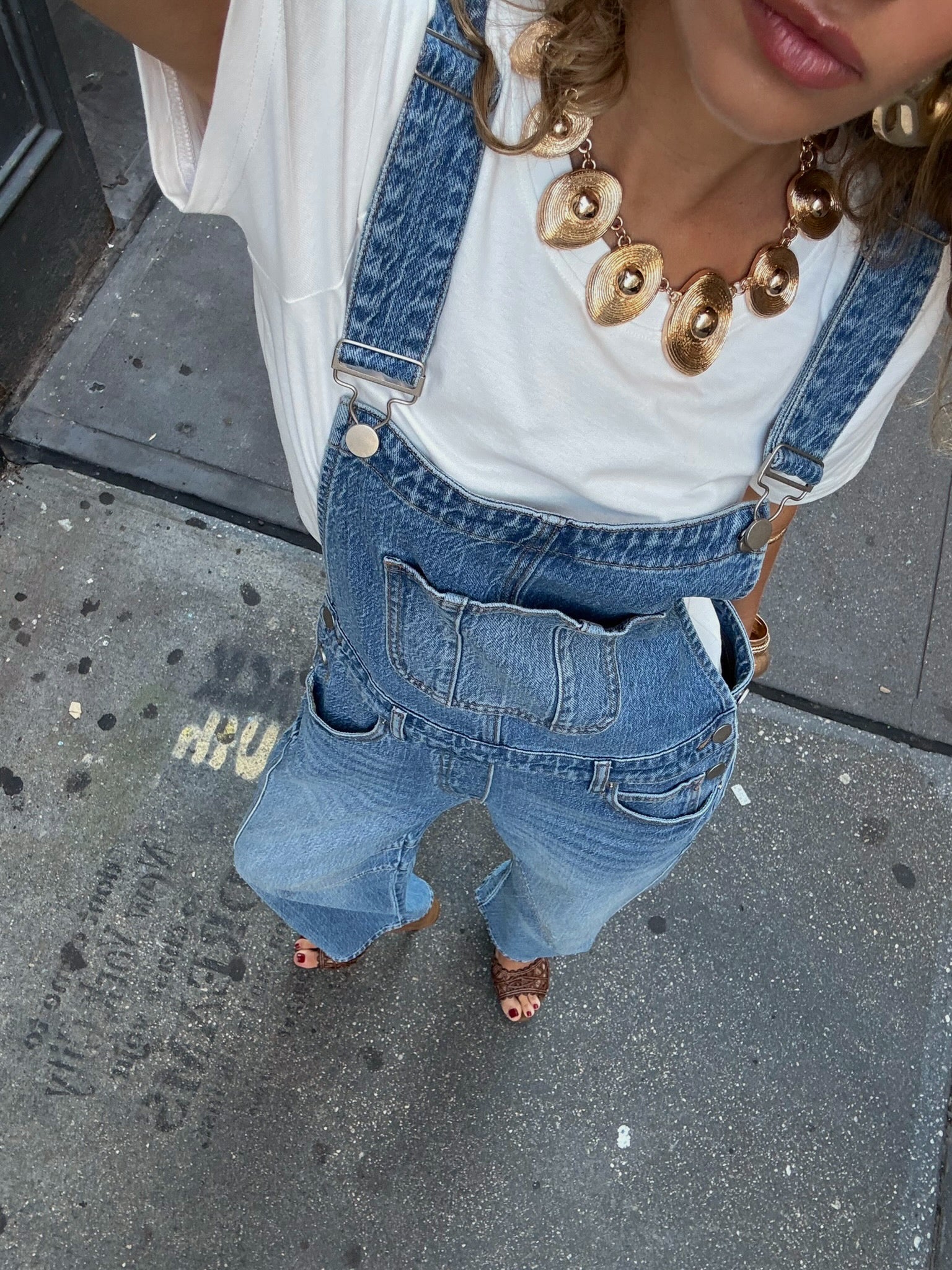 Woman wearing light-wash denim overalls over a white t-shirt with a chunky gold necklace