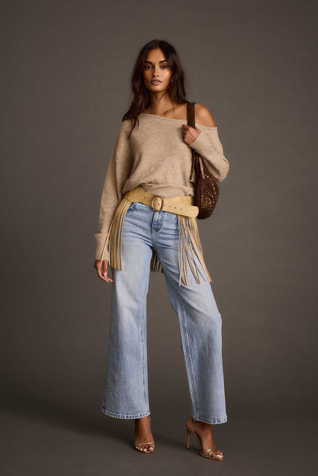 Woman wearing a camel faux suede fringe belt with a sweater, jeans, and a shoulder bag
