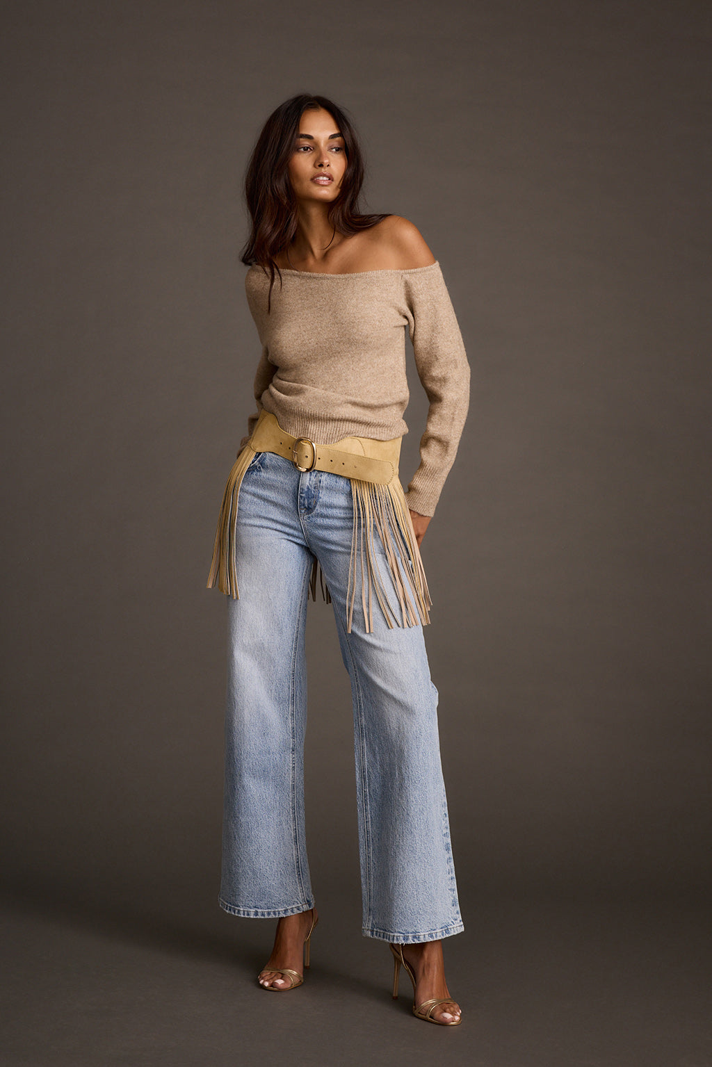 Full-length view of a woman styling a camel faux suede fringe belt with wide-leg jeans and heels