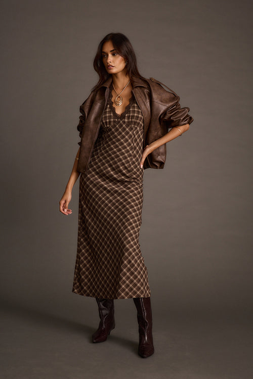 Woman wearing an espresso satin midi dress in a plaid print, layered with a brown leather jacket and boots