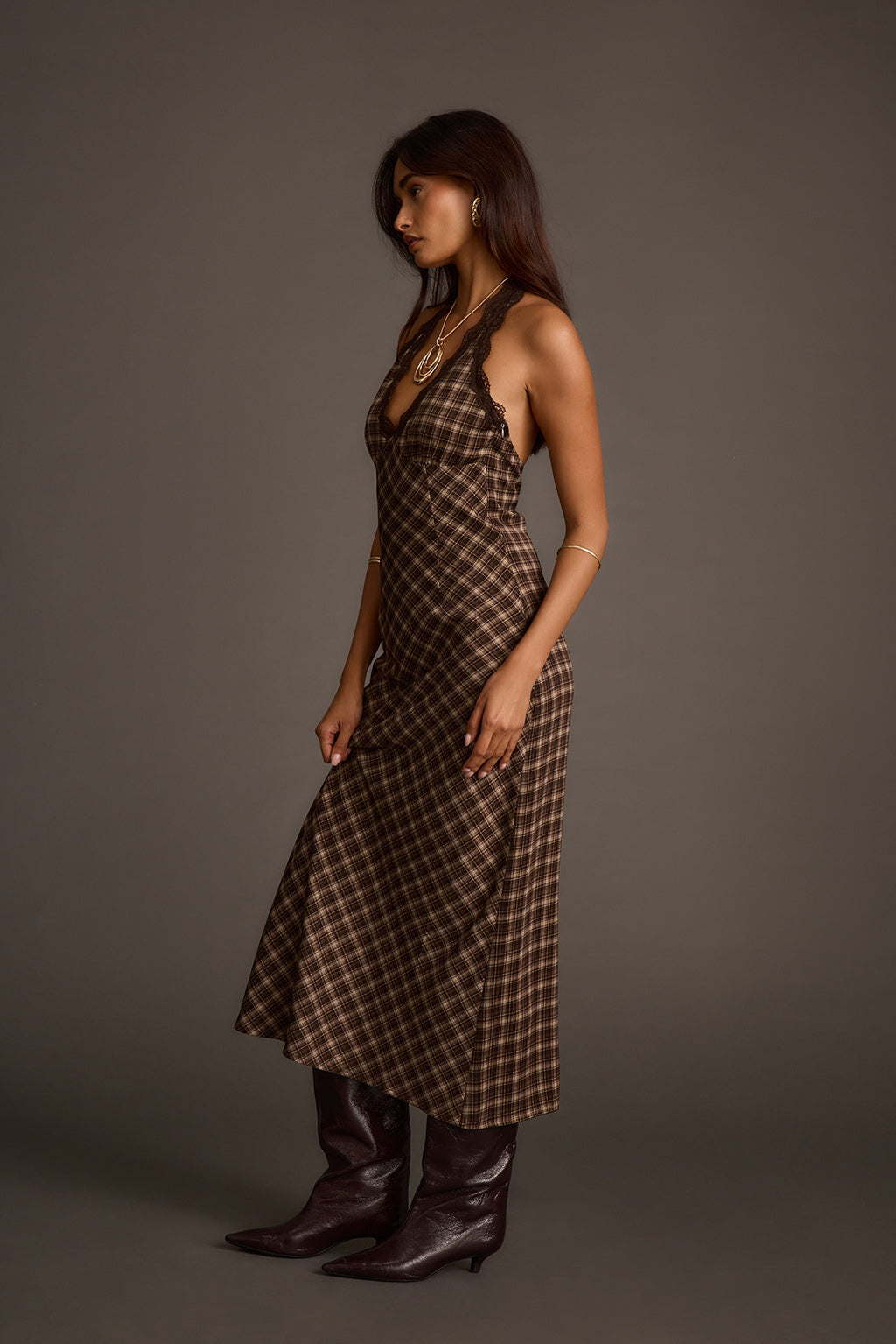 Side profile of an espresso satin midi dress with a halter neckline and layered necklaces