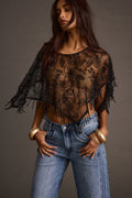 Front view of a sheer black fringe shawl top with gold bracelets and blue jeans