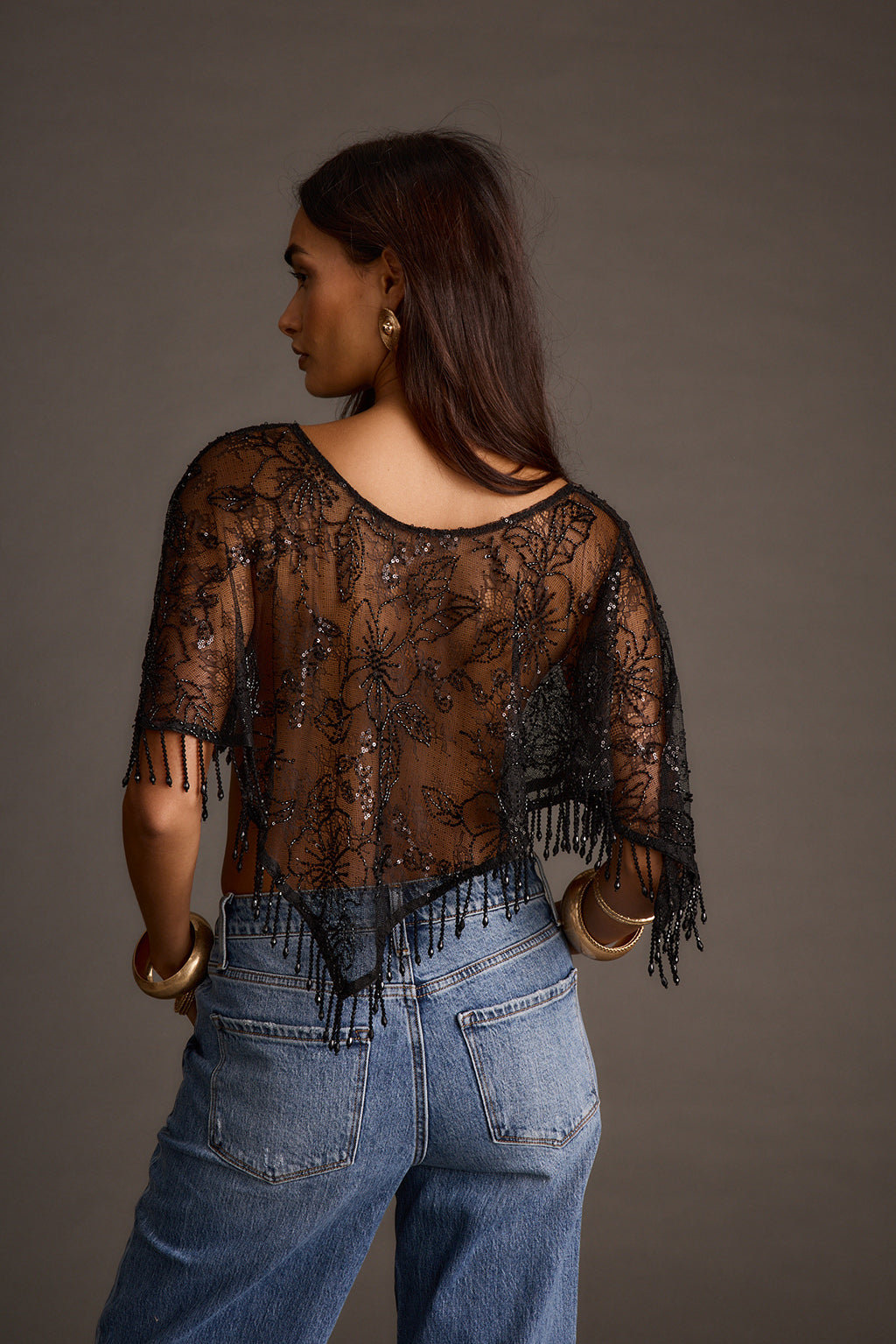 Full back view of a sheer black fringe shawl top with floral sequin detail over jeans