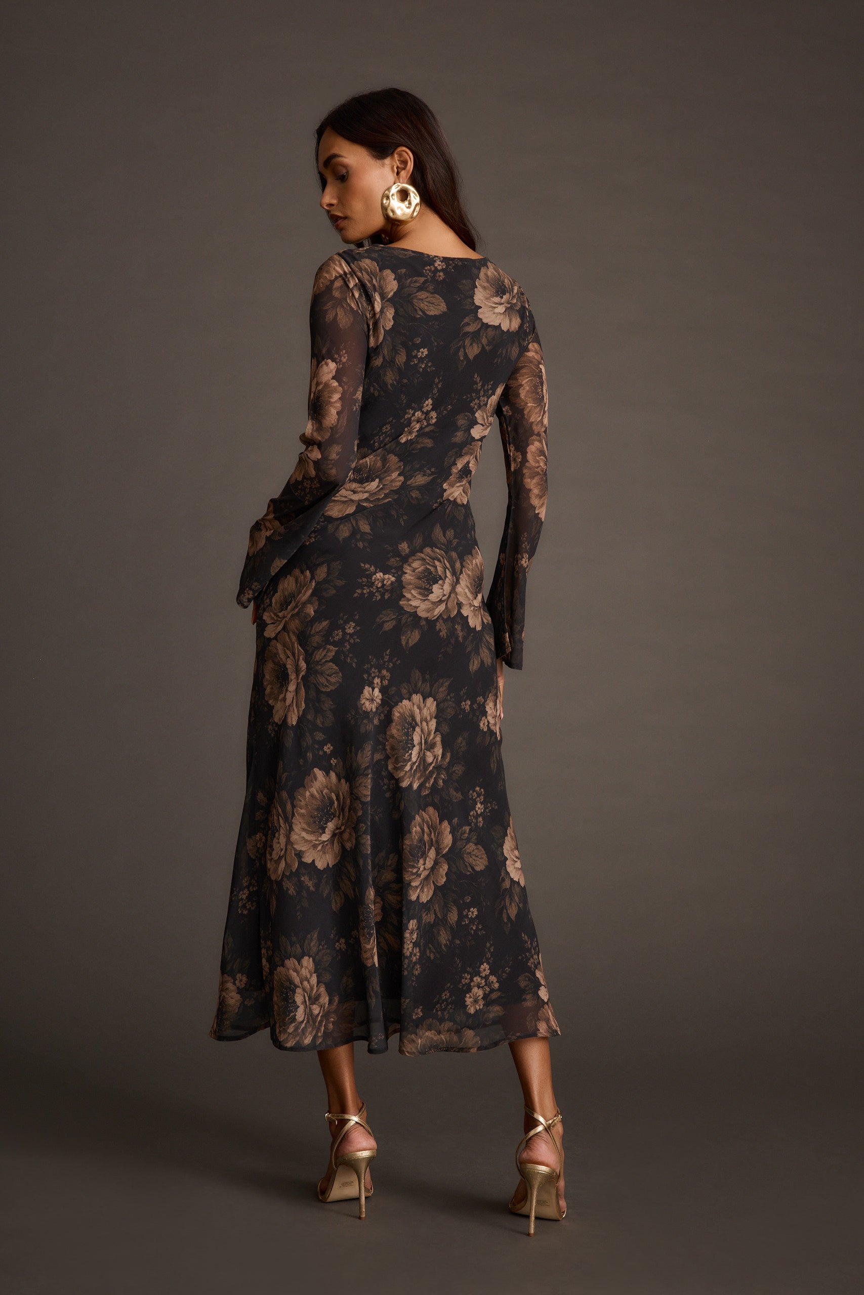 Back view of a woman wearing a floral print maxi dress with gold strappy heels