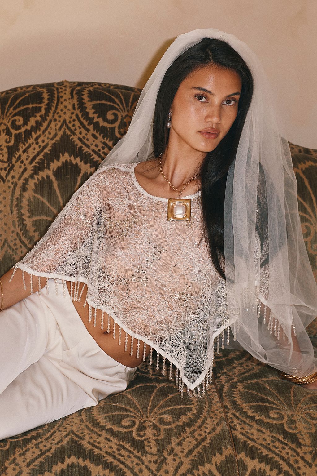Bride wearing a sheer white lace fringe shawl top with a veil and a gold pendant necklace