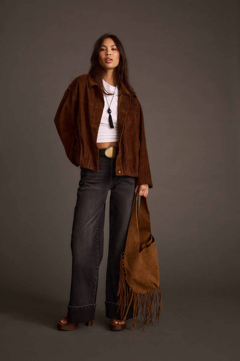 Woman wearing a mocha corduroy jacket with wide-leg jeans and a fringed suede bag