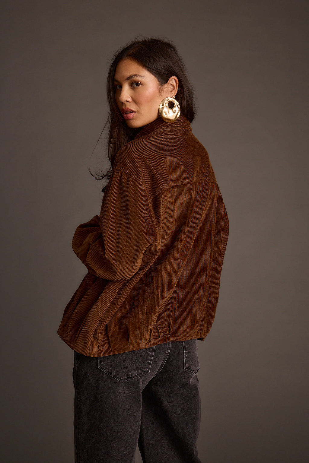 Back view of a mocha corduroy jacket highlighting its relaxed silhouette and gold hoop earrings