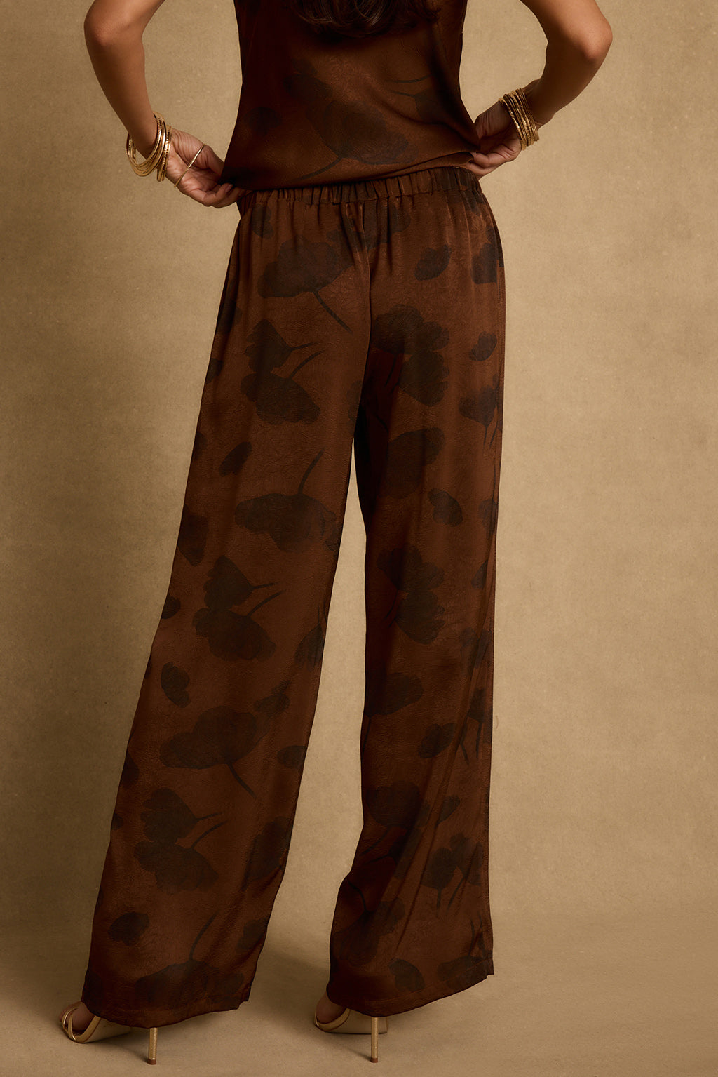 Back view of espresso brown floral satin pants with elastic waist and wide legs.