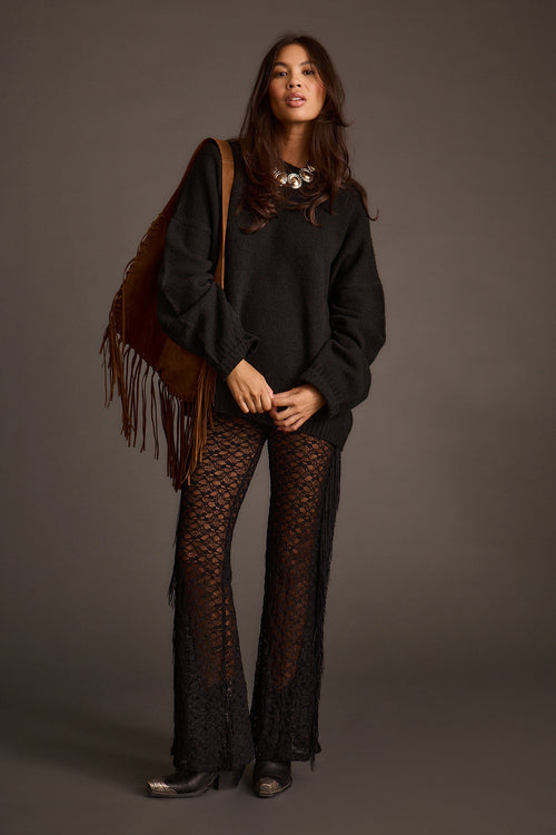 Woman wearing a black oversized sweater with crochet flared pants and a fringed shoulder bag