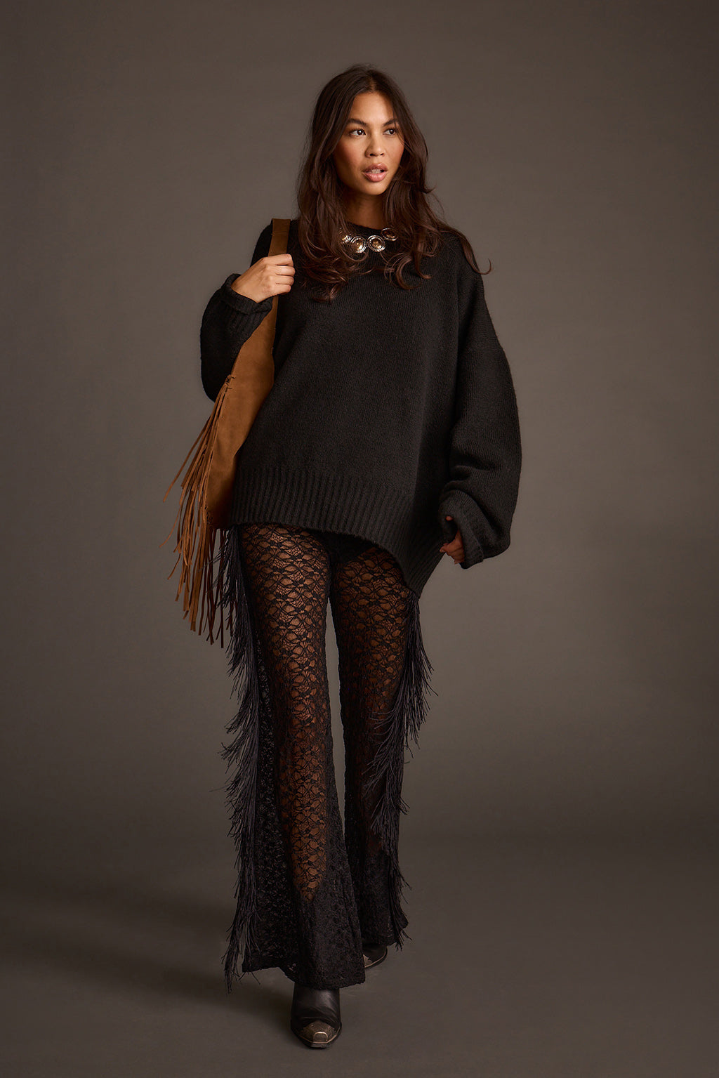 Model walking in a black oversized sweater with sheer crochet flared pants and a fringed bag