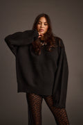 Close-up of a woman wearing a black oversized sweater with a ribbed crew neckline and fishnet tights