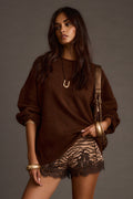 Woman wearing a brown oversized sweater with lace-trimmed shorts and a gold shoulder bag