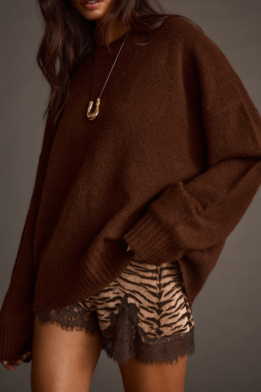Cropped view of a brown oversized sweater paired with a gold pendant necklace